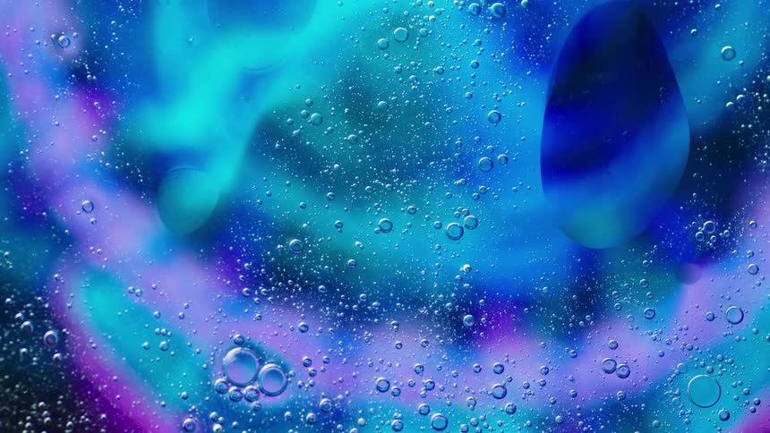 Blue and purple lights glow as bubbles move in a clear liquid substance and reflect the color and light