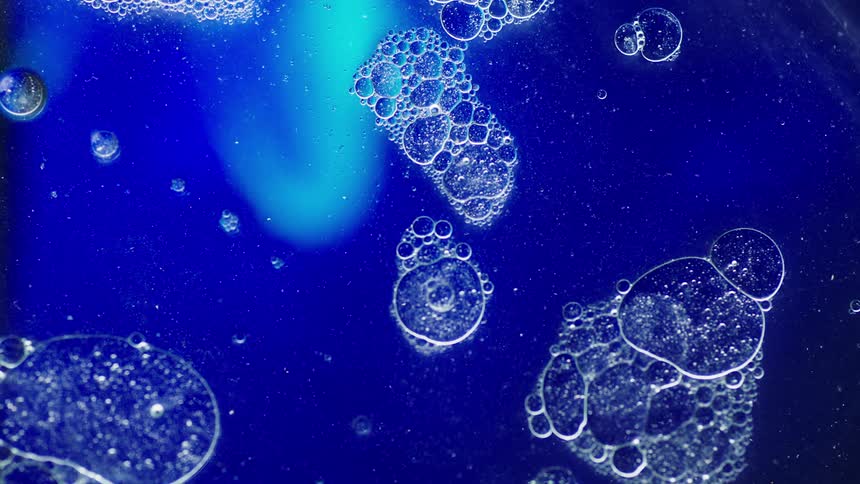 Several groups of bubbles are floating atop a liquid with a blue hue
