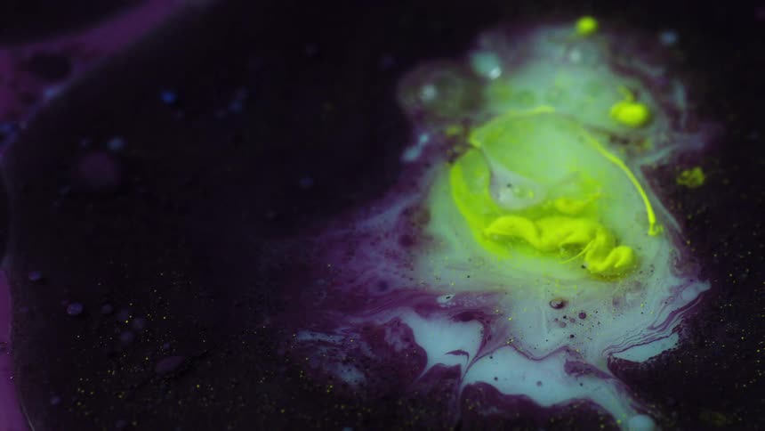 A close up of yellow paint being dropped into a liquid substance