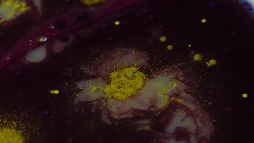 A colored fluid has a small cluster of greenish droplets suspended on its surface