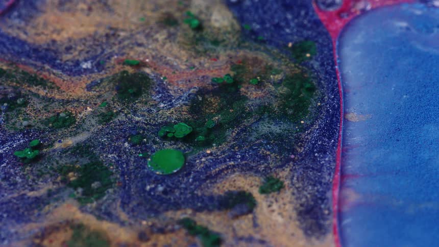 Green and tan sand and green disks flow on surface of blue and pink mixture