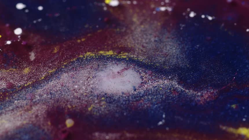 An up close of liquid being dropped in colorful paint causing ripples