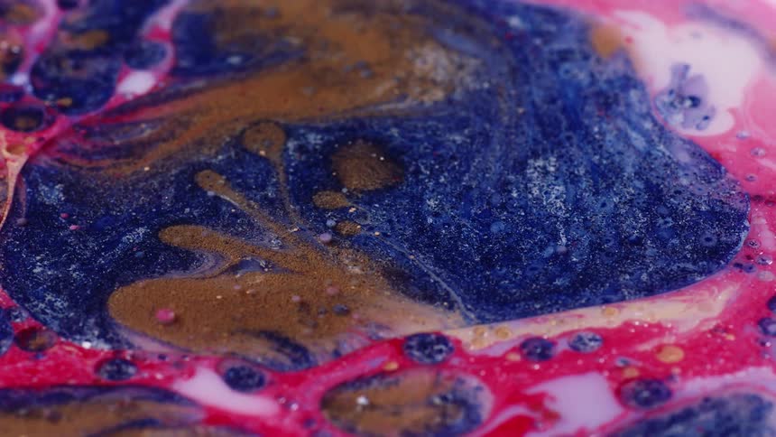 Abstract close up of pink blue gold white and glitter paints oil and water based swirling around