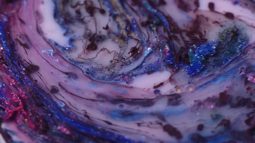 A liquid of many different shades with glitter suspended in it swirls around