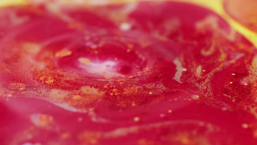 Red and yellow paint being mixed together and dropped into creating ripples in the paint