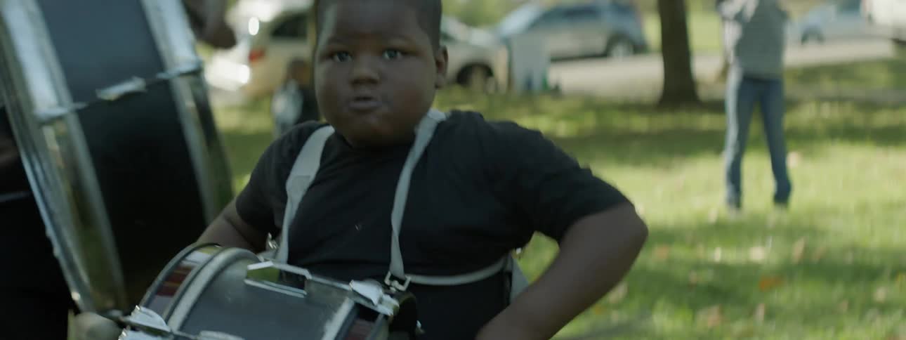 Boy drumming on a snare drum outside with other drummers
