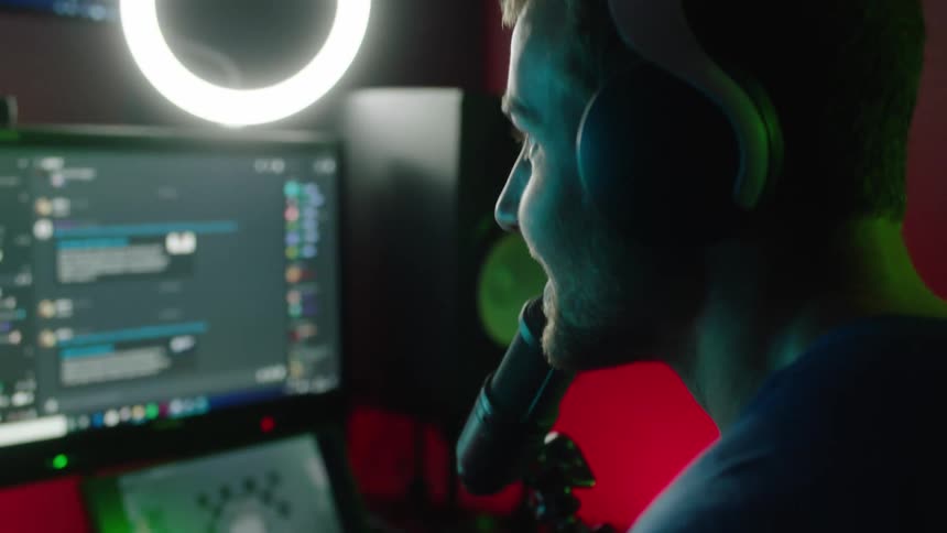 Man wearing headphones records while looking at monitors and speaking into microphone