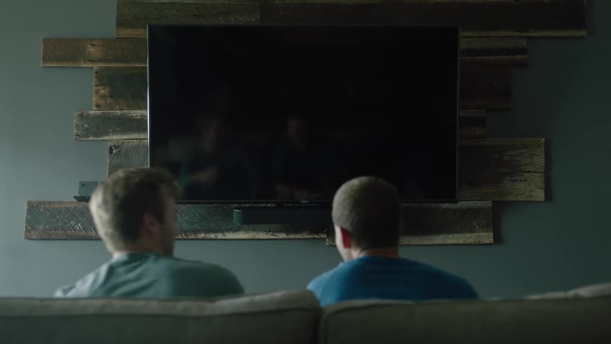 Two teens are sitting down and watching television