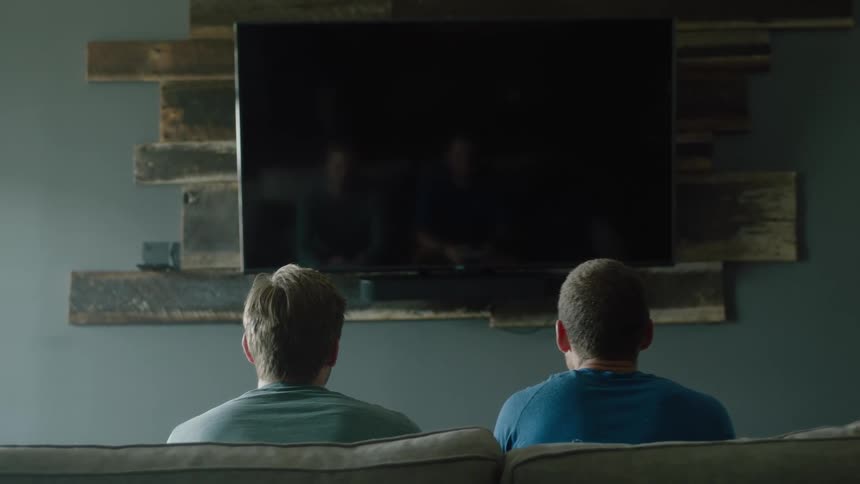 Two men sitting on a couch in front of a television moving side to side