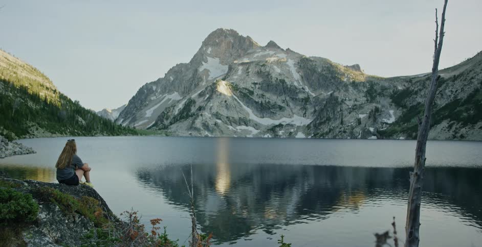 A young woman is sitting down and looking at the lake in the day time