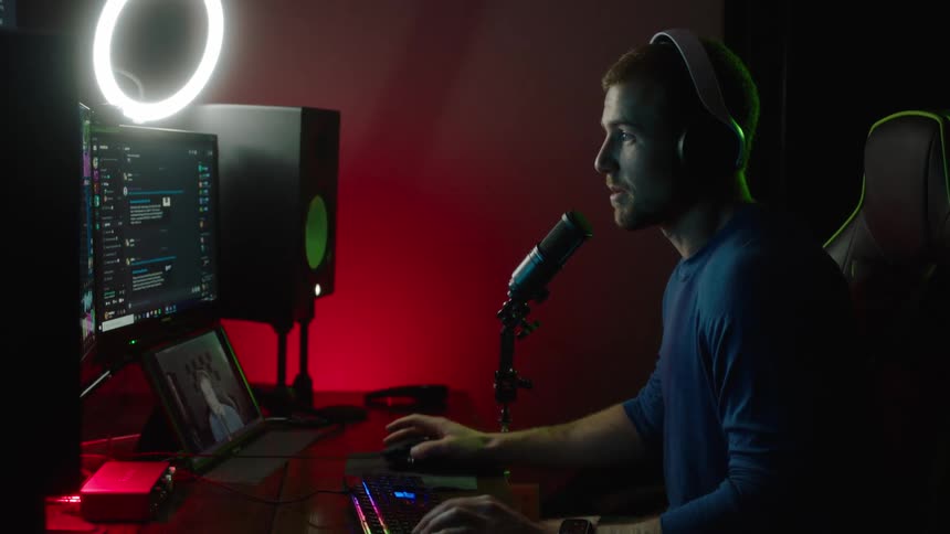 A man sits at his computer while speaking into a microphone at his desk