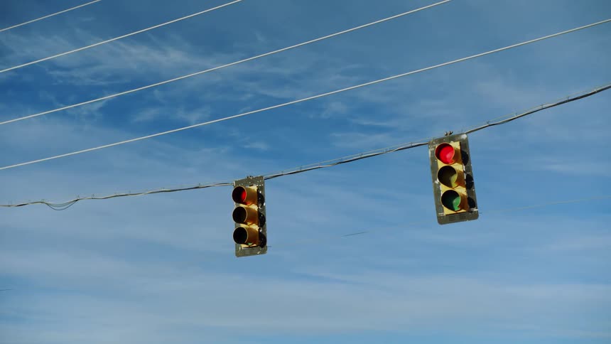 A pair of traffic lights hanging from a cable change color from red to green