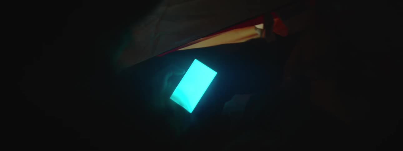 Woman uses smartphone in tent at night