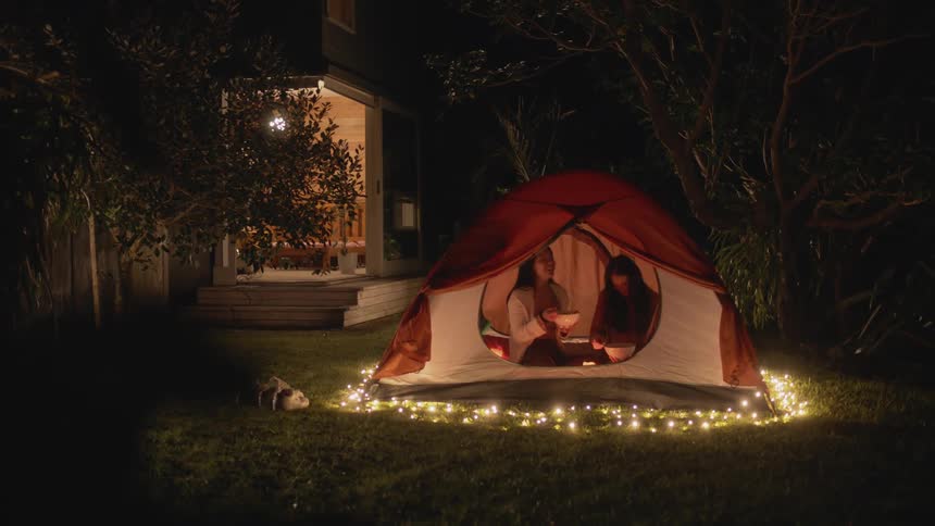 Two friends are camping outside of a tent at night time