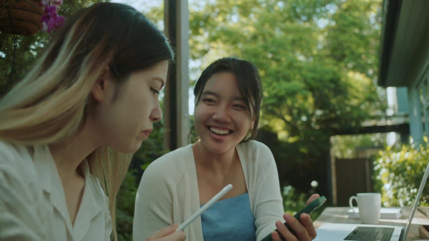 Two women are sitting outdoors with their laptops