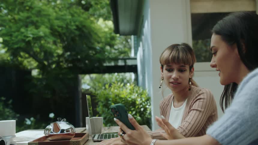 Two woman sitting next to each other looking at a phone and talking