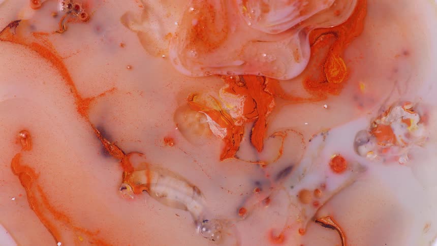 Orange and white paint being mixed together creating swirls and bubbles
