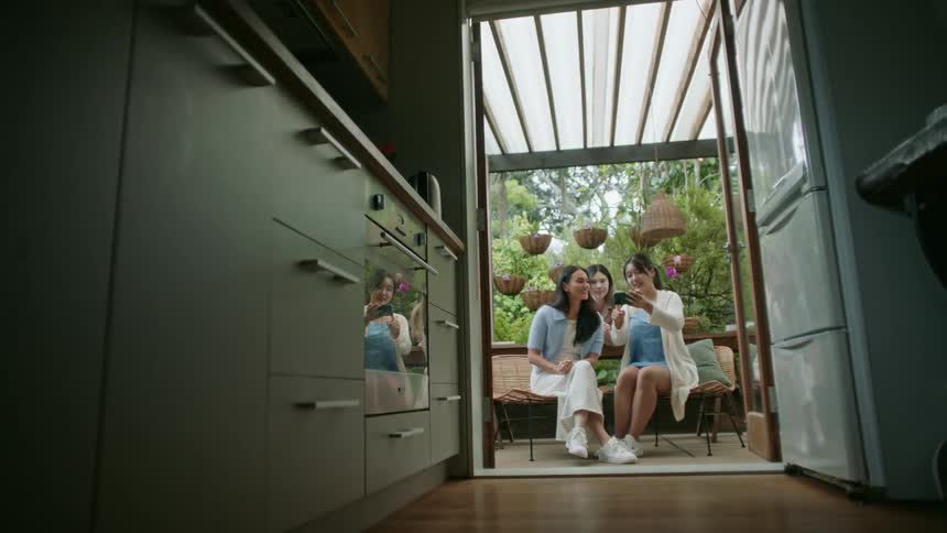 Three women sitting outside posing for a picture on a womans cellphone