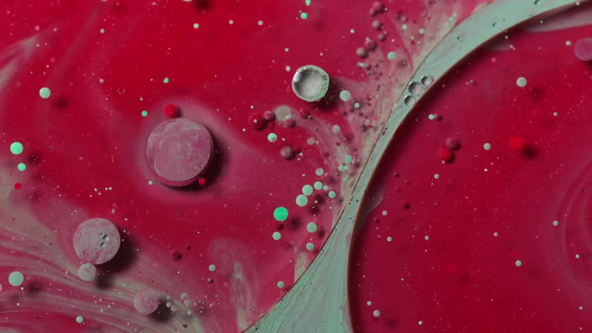 A green stripe stretches through a red substance as green and red orbs float on the surface as it moves