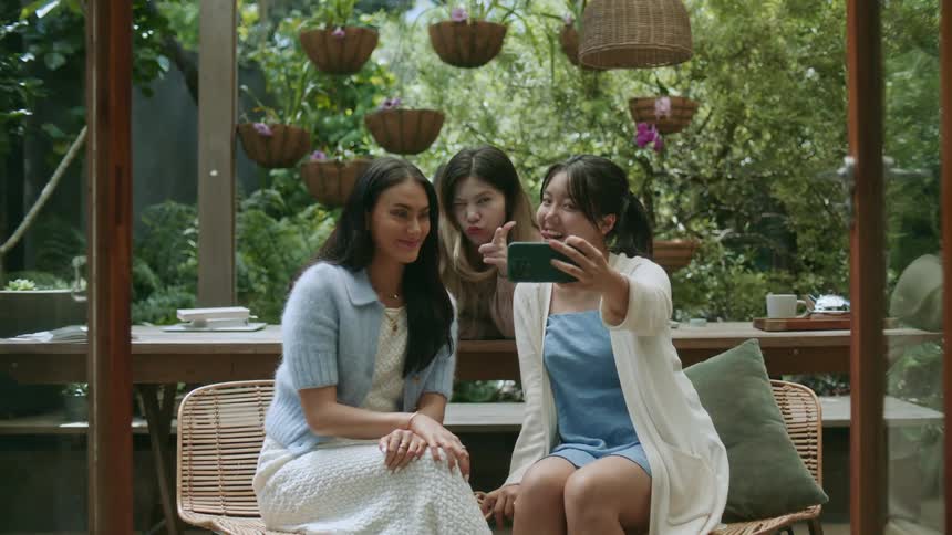A group of women pose together for a selfie before laughing while sitting together outdoors during the day