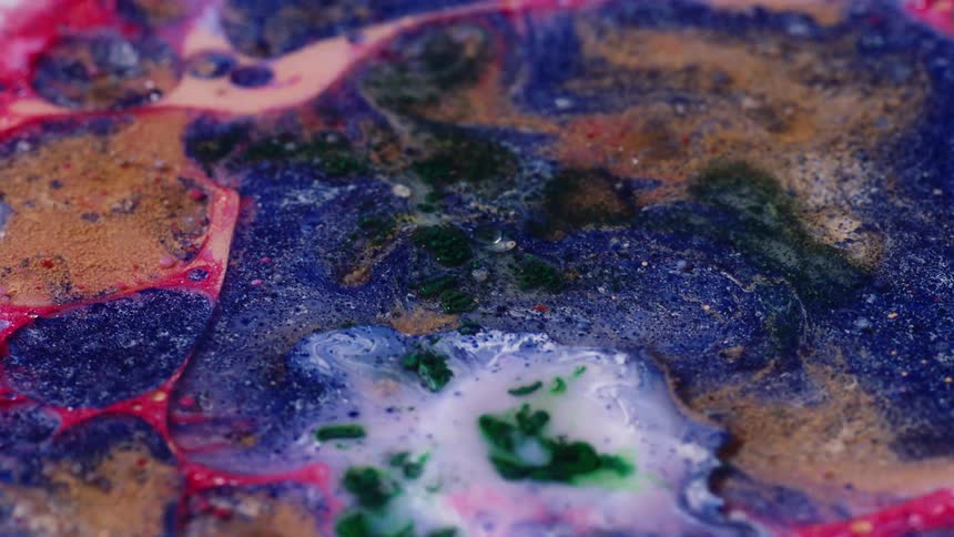 Many colors in liquid move and spread as droplets fall and the substance ripples