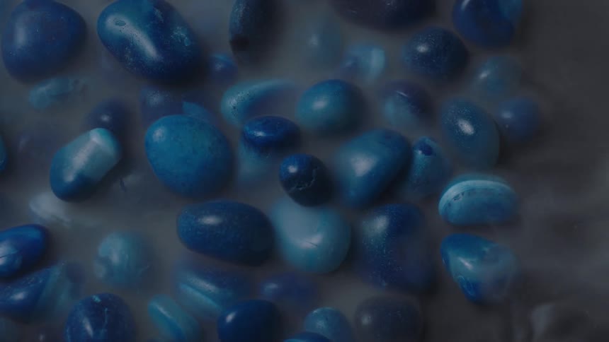 Smoke moves blue pebbles glued onto a murky substance