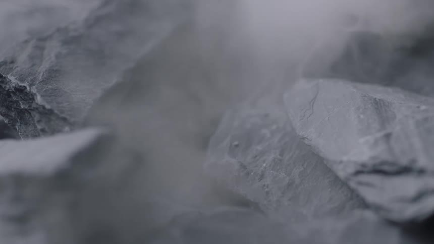 Pieces of jagged gray rock fall and create a small cloud of dust