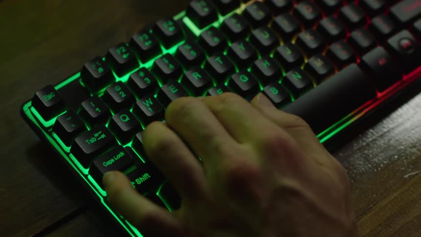 Close up of a mans hands as he types on an illuminated keyboard repeatedly