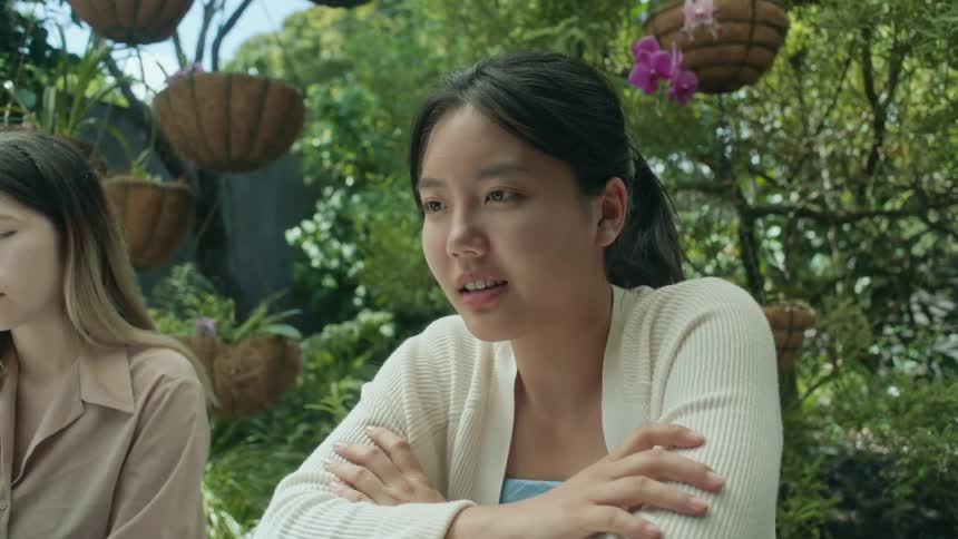 Woman sitting outdoors near several hanging plants with another woman smiles while viewing computer screen