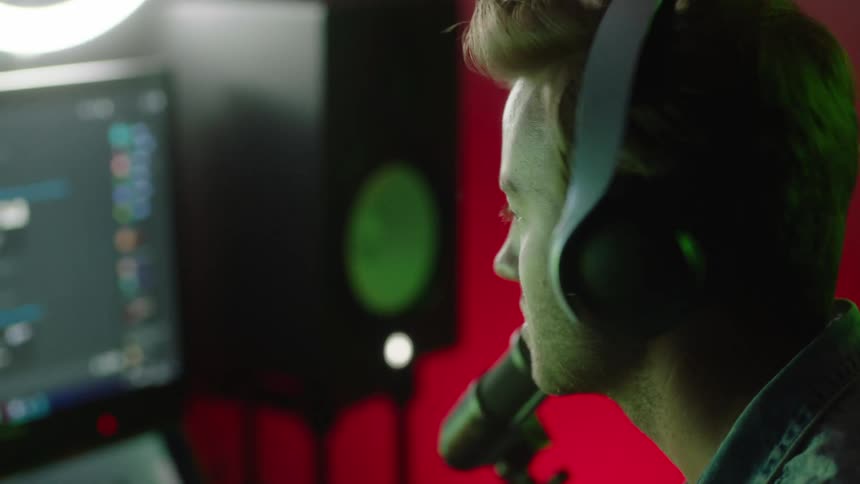 A man sitting at his computer desk picks up headphones and puts them on