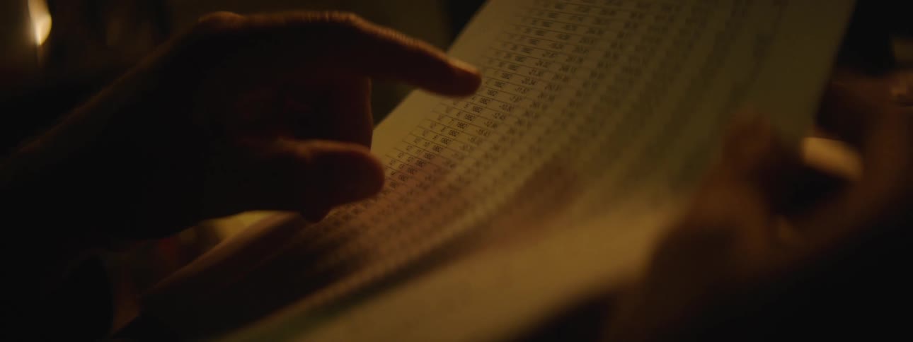 A person is sitting indoors and reading a piece of paper