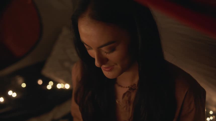 Close up of a girl surrounded by candles on a dimly lit room talking to a friend