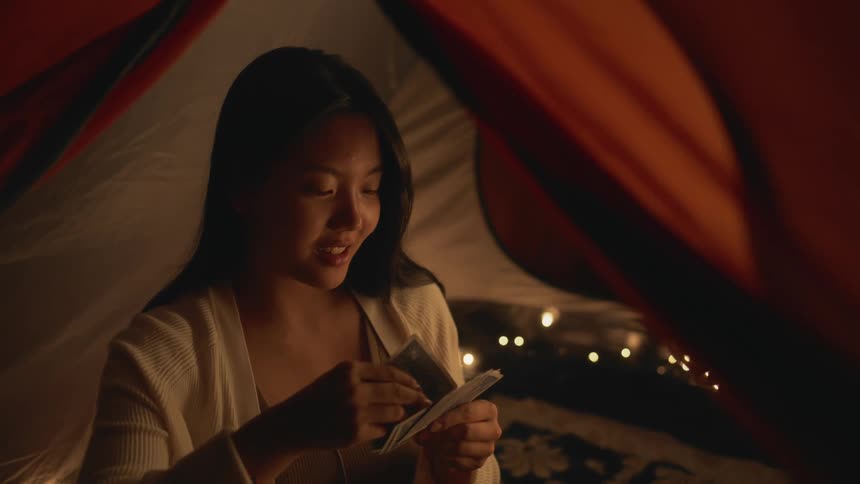 A young woman plays cards while sitting in a tent