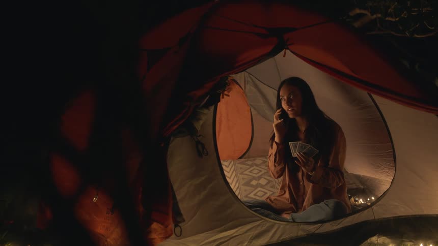 A young woman is inside of her tent and is talking on the phone