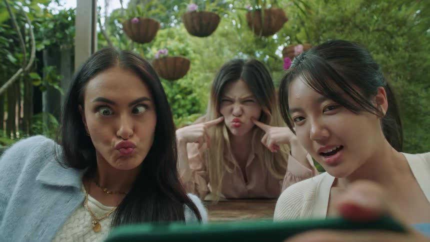 A group of three female friends are taking selfies outside and making funny faces like sticking their tongues out at the camera phone