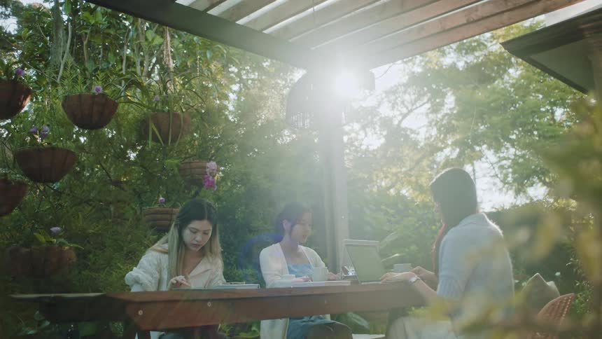 Three women sitting at a table two typing on a laptop and another writing