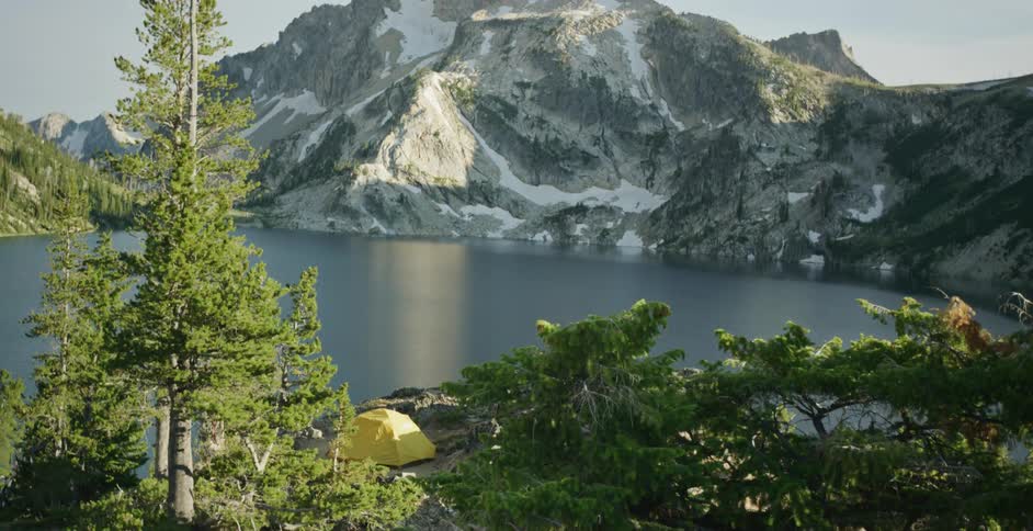 Yellow tent set up on the shores of a lake near the snow covered slopes of a mountain at morning