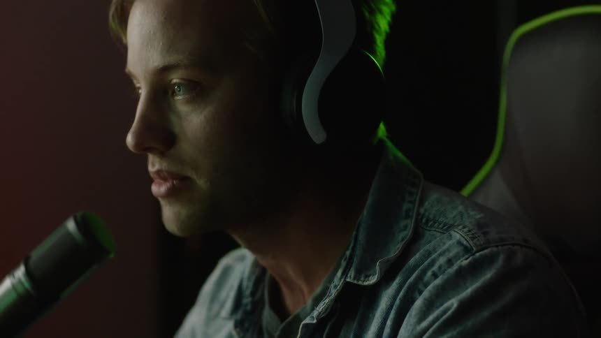 A man wearing headphones is sitting in a chair speaking into a microphone and he raises his arms into the air