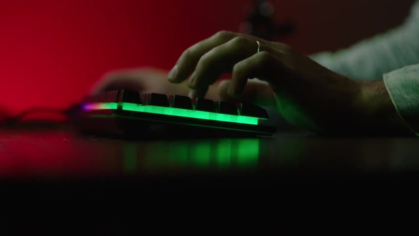 The hands of a male are shown typing on a computer keyboard sitting on a desk
