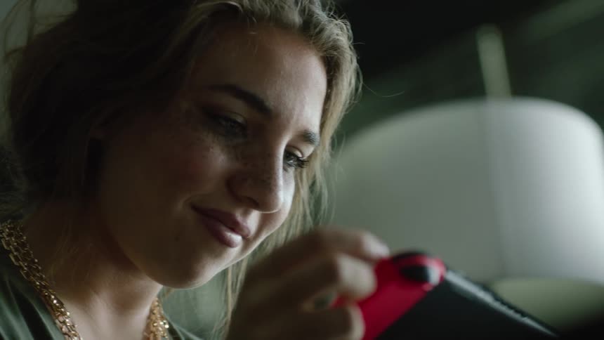 A young woman playing on a nintendo switch shakes her fist in excitement