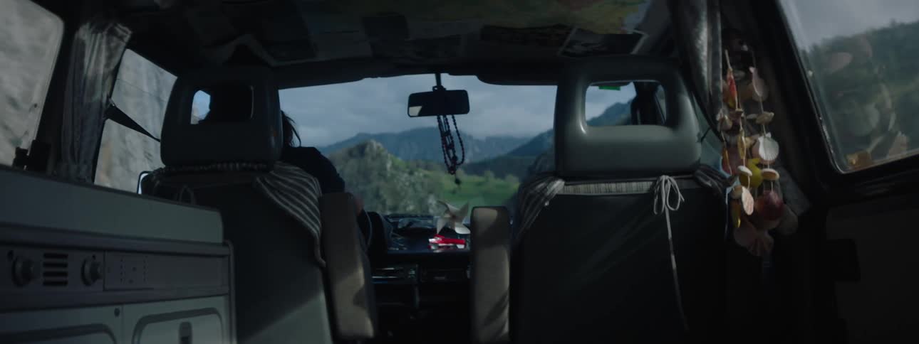 A man in a van drives along a mountainous road on a sunny day