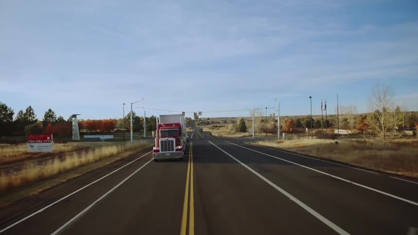 A big red semi truck is traveling among traffic on a rural highway on a beautiful autumn day