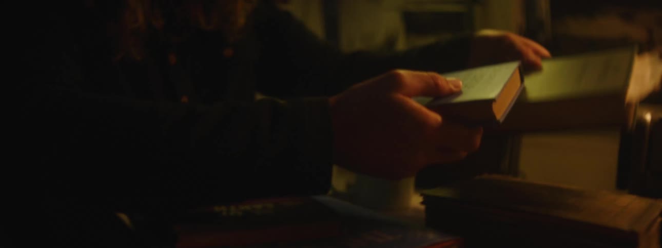 A bearded man with long hair quickly looks through a stack of books