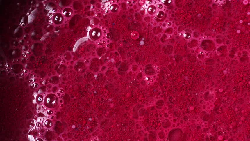 Top down close up of air bubbles breaking the surface of a pool of red liquid ink