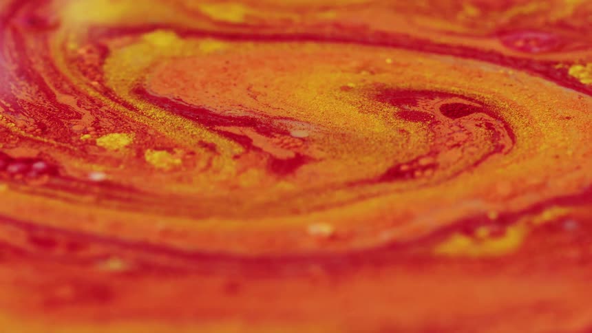 A red yellow and orange textured liquid surface swirls as it blends and moves