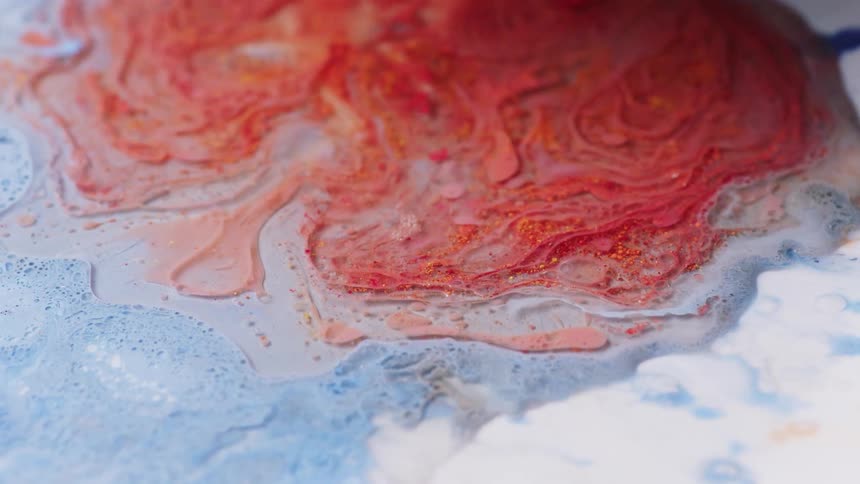 Close up of bright red liquid ink pouring over a surface covered with light blue ink