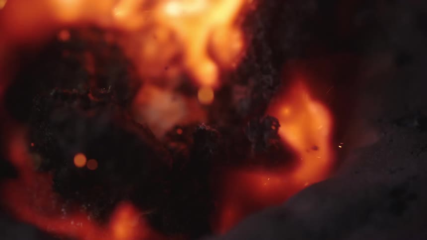 Flames move and sparks fly as a fire burns on charred wood
