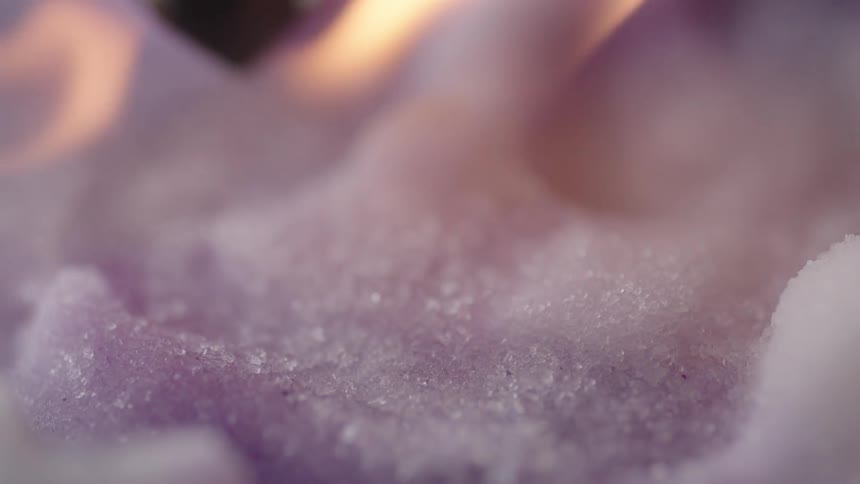 Extreme close up of a yellow flame hovering over the surface of a purple candy like surface