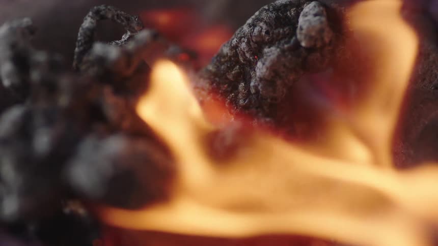 A fire flickers as it gently burns away and leaves charred material beneath it