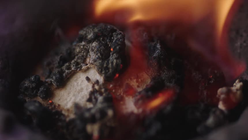 Extreme closeup of burning marshmallow with charred edges and embers